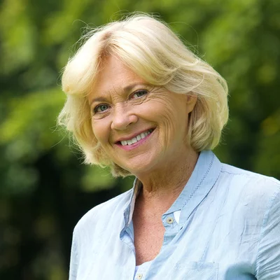 Vorwerk: Foto: Eine Frau mit blonden Haaren steht in einem Park und lächelt.