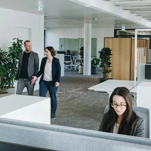 Vorwerk: Foto: Hier ist eines der Grp0ßraumbüros abgebildet. Eine Vorwerkerin arbeitet an einem der Schreibtischplätze, zwei Personen gehen über den großzügigen Gang.