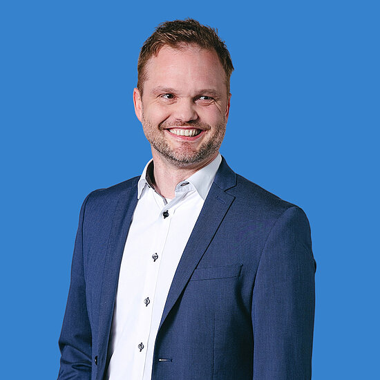 Vorwerk: Photo: A man in a white shirt and blue jacket smiles at the camera.