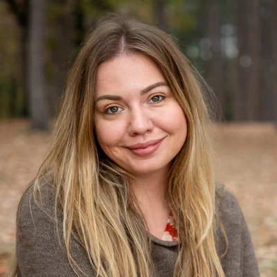 Vorwerk: Foto: Eine Frau sitzt auf dem Boden in einem Park und lächelt, umgeben von Bäumen.