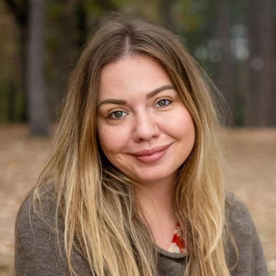 Vorwerk: Foto: Eine Frau sitzt auf dem Boden in einem Park und lächelt, umgeben von Bäumen.