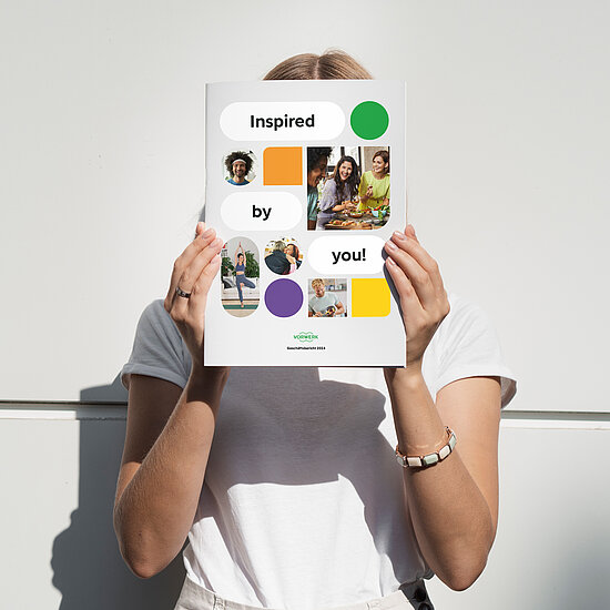 Vorwerk: Photo: A woman in a white T-shirt holds our printed annual report in front of her face. You can see the cover page.