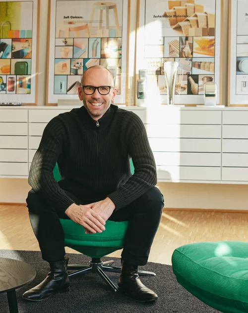 Vorwerk: Foto: Der Vorwerk Chefdesigner Jan Delfs sitzt breitbeinig auf dem grünen Sessel und strahlt frontal in die Kamera.