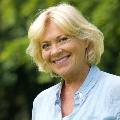 Vorwerk: Foto: Eine Frau mit blonden Haaren steht in einem Park und lächelt.