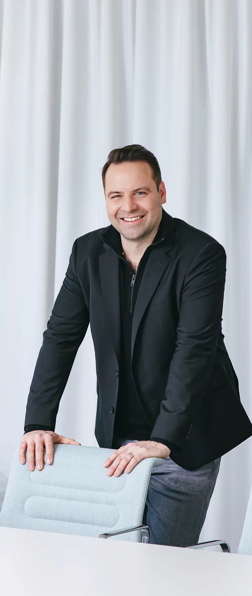Vorwerk: Foto: Der Mann im schwarzen Sakko zur Jeans, der sich auf einer Stuhlrückenlehne abstützt und in die Kamera lächelt, ist Julius Ganns, der bei Vorwerk für Software und Digitales verantwortlich ist.