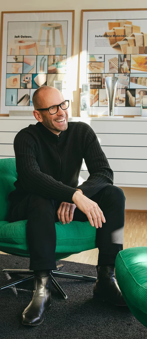 Vorwerk: Foto: Das Foto zeigt Jan Delfs, den Chefdesigner von Vorwerk. Ganz in Schwarz gekleidet, sitzt auf einem grünen, modernen Sessel und lacht.