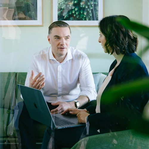 Vorwerk: Foto: Eine Frau und ein Mann sitzen in einer Plauderecke zusammen und unterhalten sich. In der Mitte steht ein Laptop.