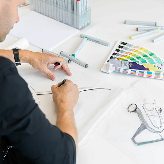 Vorwerk: Photo: A man is busy with a design project, working intently at a desk filled with design tools and digital devices.
