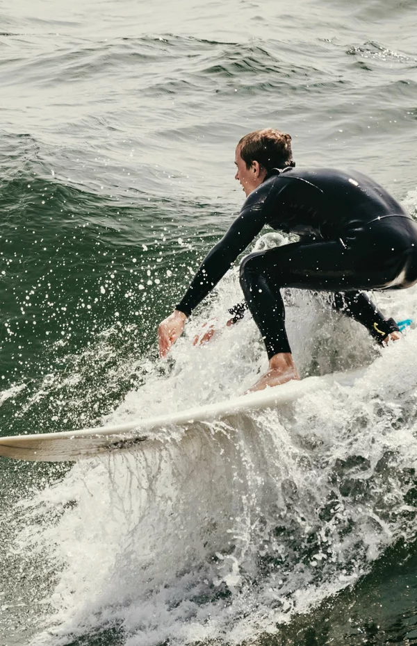 Vorwerk: Foto: Ein Surfer im Neoprenanzug auf seinem Surfbrett in einer großen Welle im Meer.